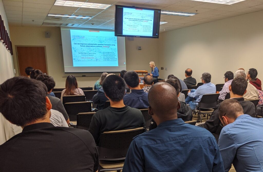 A photo of Eugenia Kalnay presenting to a packed room of participants