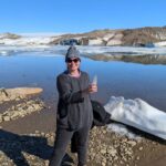 Zamora stands in front of the corner of the Greenland ice sheet. The ice is melted as the photo is taken in August. Zamora is posing with a piece of ice in her hand.