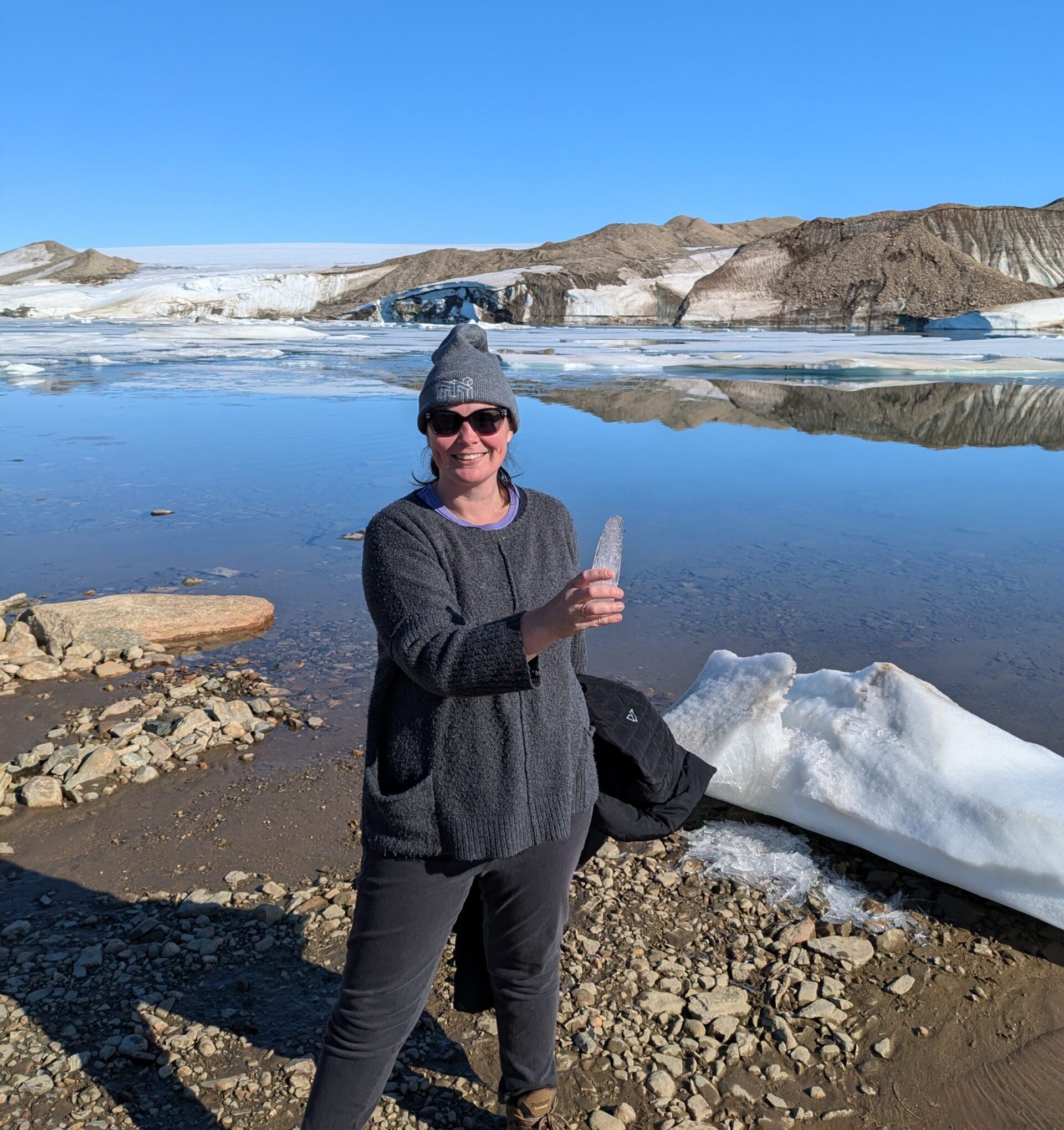 Zamora stands in front of the corner of the Greenland ice sheet. The ice is melted as the photo is taken in August. Zamora is posing with a piece of ice in her hand.