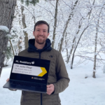 Justin stands in front of a wintery scene holding a laptop