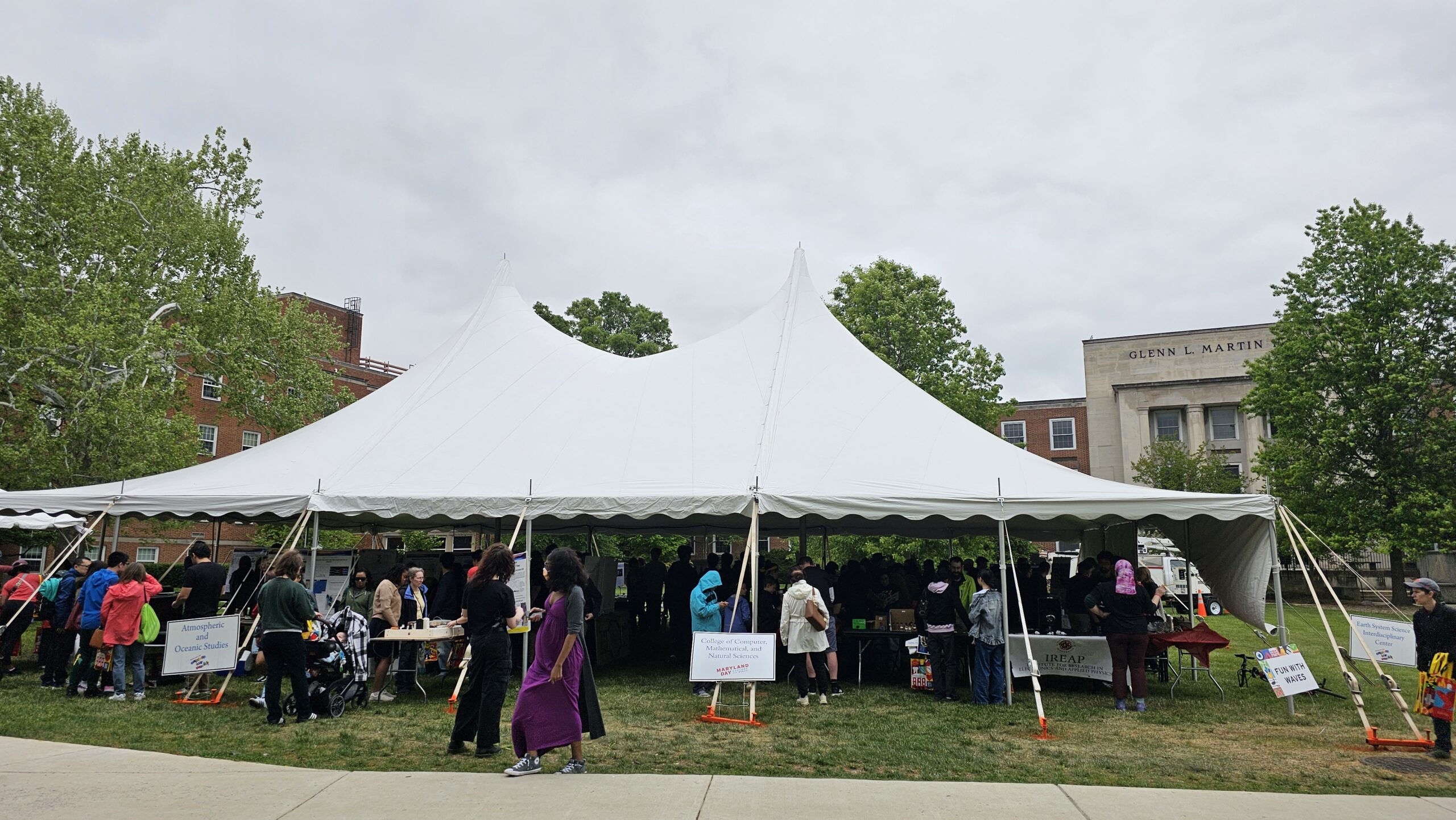 A large white tent on the grass in front of the Glenn L. Martin building, hosting several CMNS departments