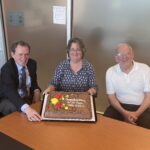 Maureen Cribb holds up an anniversary cake and sits with Lars Peter Riishojgaard and Andy Negri