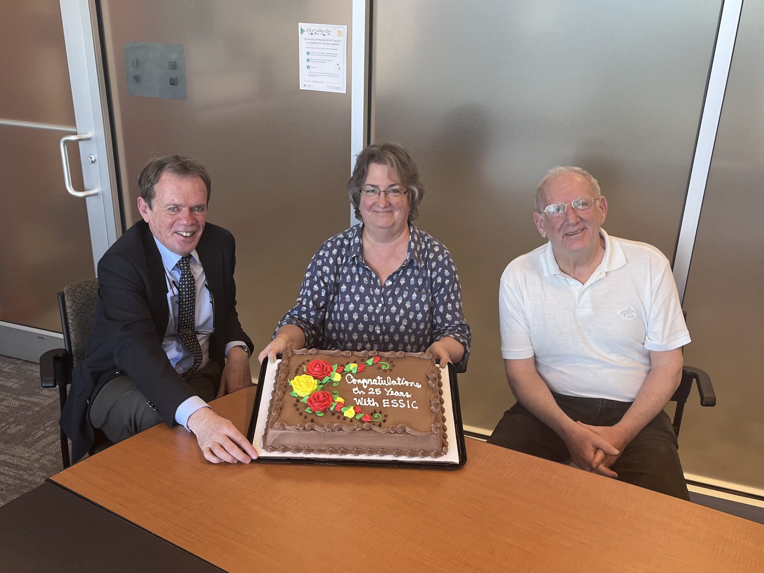 Maureen Cribb holds up an anniversary cake and sits with Lars Peter Riishojgaard and Andy Negri
