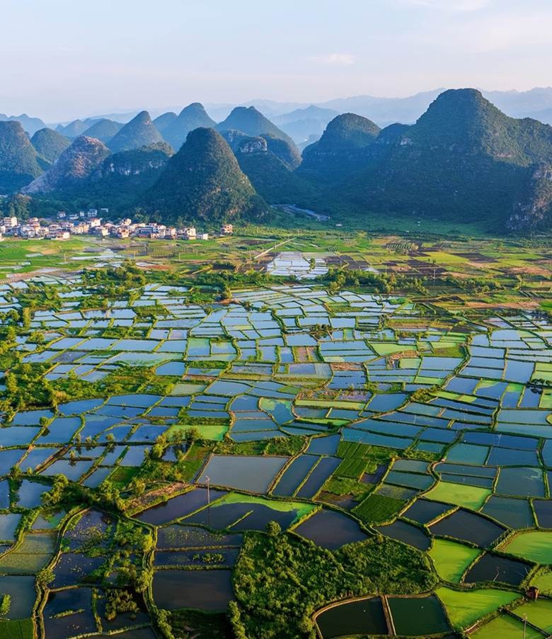 Flooded rice paddies make a grid in a valley next to a rural village