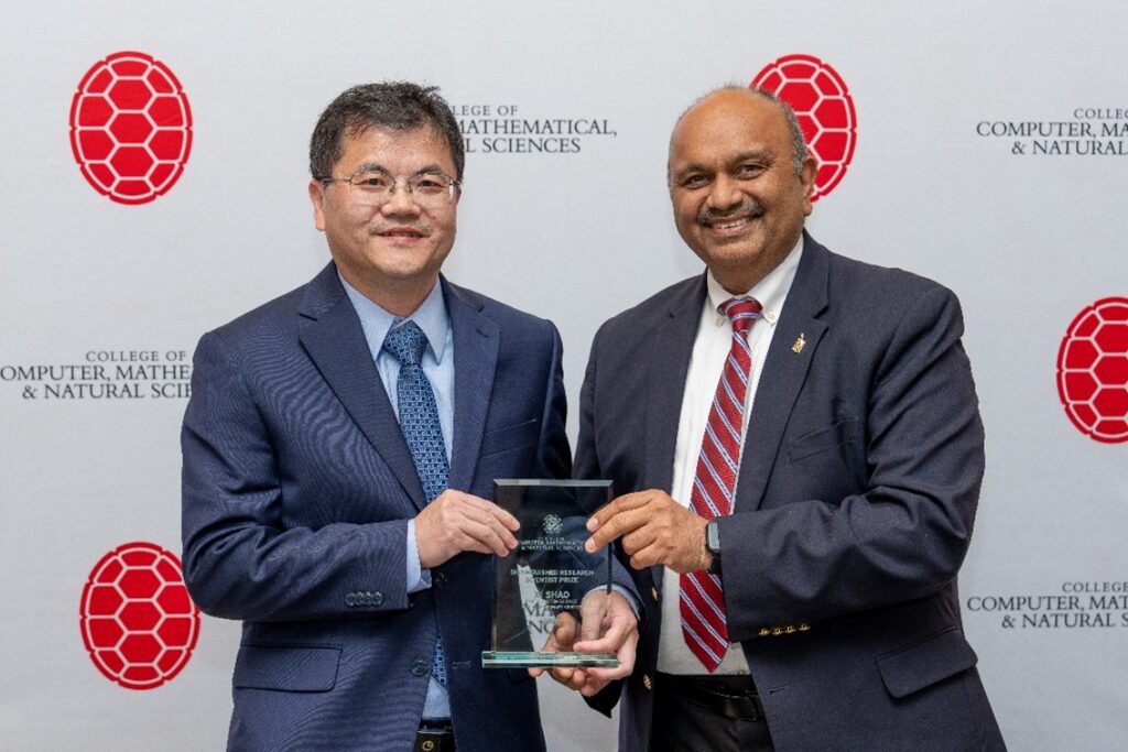 Two men pose happily holding an award