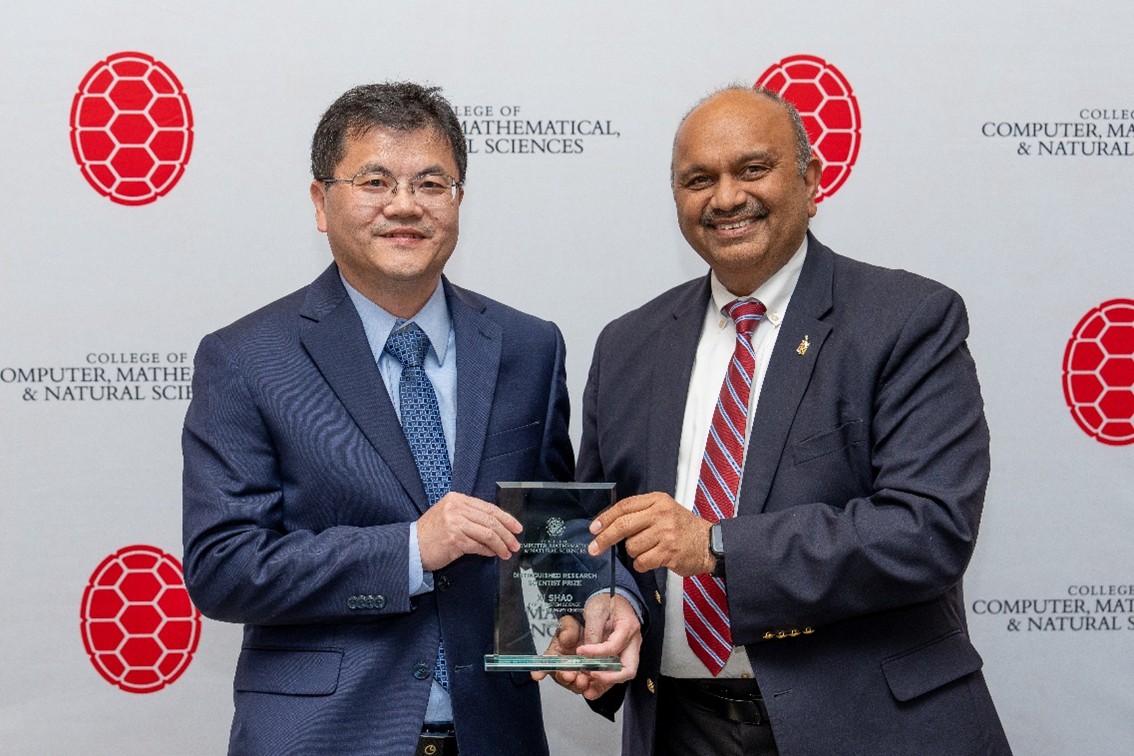 Two men pose happily holding an award