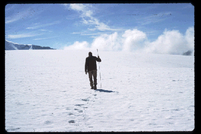 A man walks away with a walking stick, silhouetted against the white snow